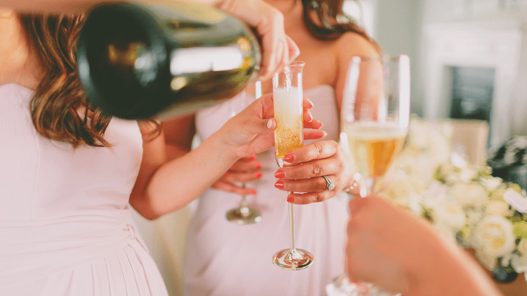 Champagne being poured into a flute held by a woman in a white dress at a celebration.